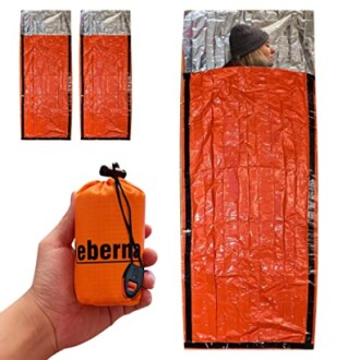 Emergency sleeping bag with orange exterior and silver interior, shown in use and compacted in hand.