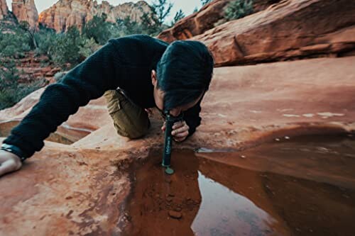 Person examining water sample in desert terrain.