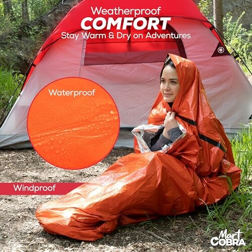 Person in orange weatherproof sleeping bag next to a tent in the woods.